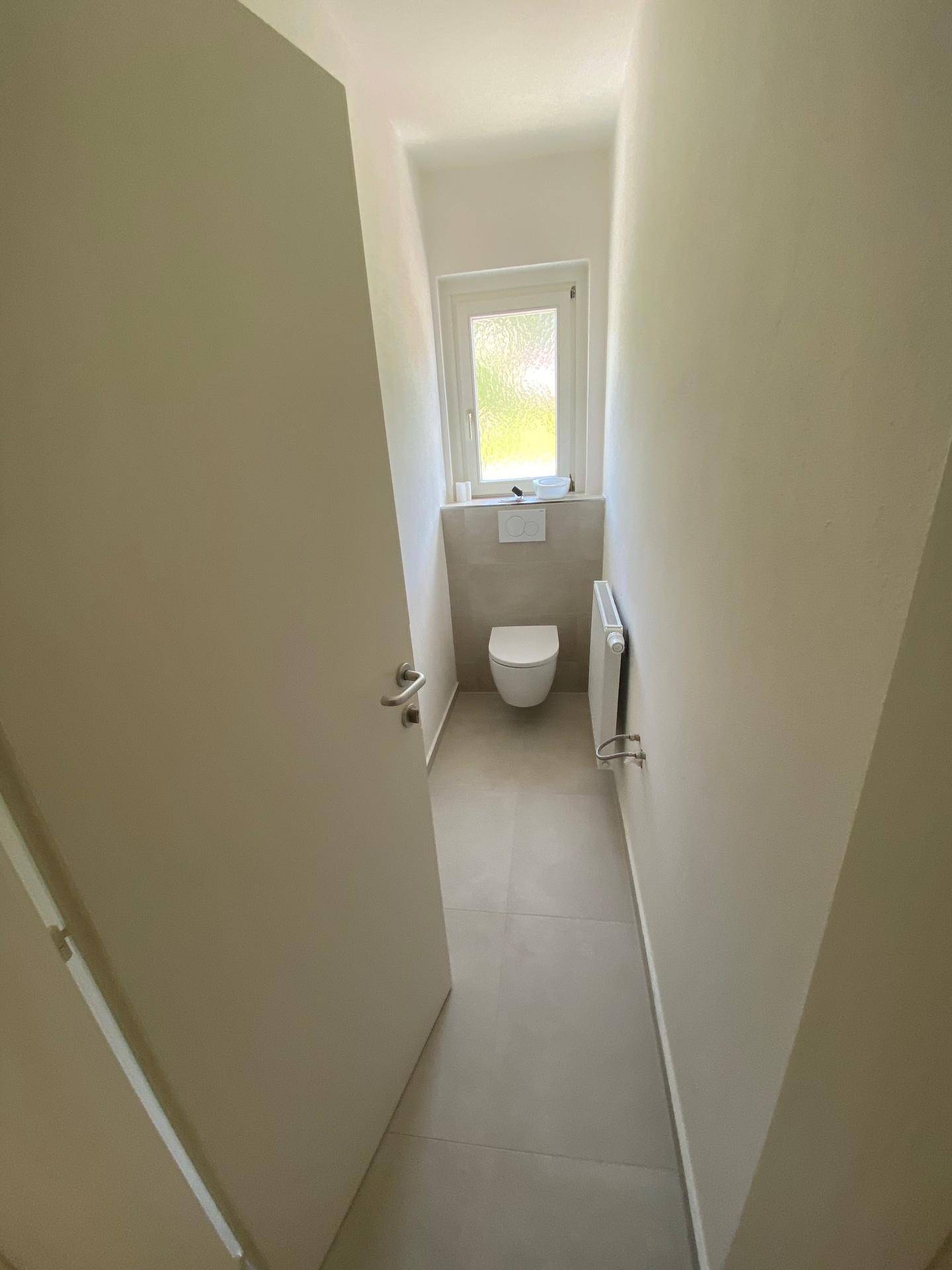 Separates Gäste-WC mit Fenster, Wand-WC und Heizkörper in einem schlichten Design.