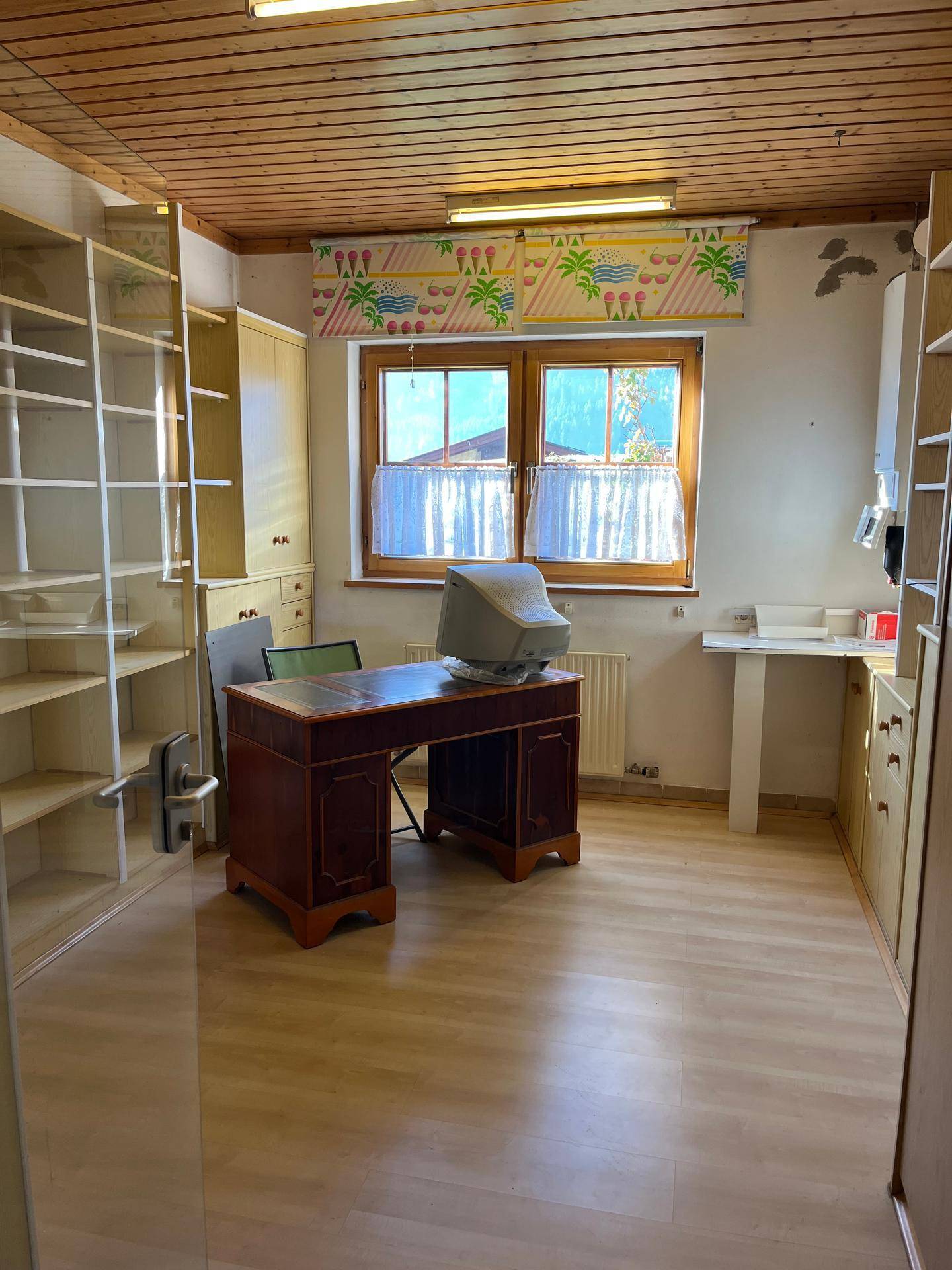 Arbeitszimmer mit Holzdecke, Schreibtisch und Regalen, das durch ein Fenster gut beleuchtet wird.