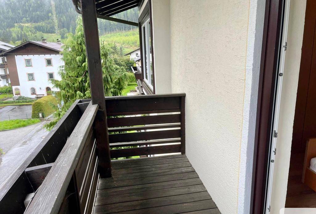 Kleiner Holzbalkon mit Geländer, der einen Blick auf die bewaldete Berglandschaft freigibt.