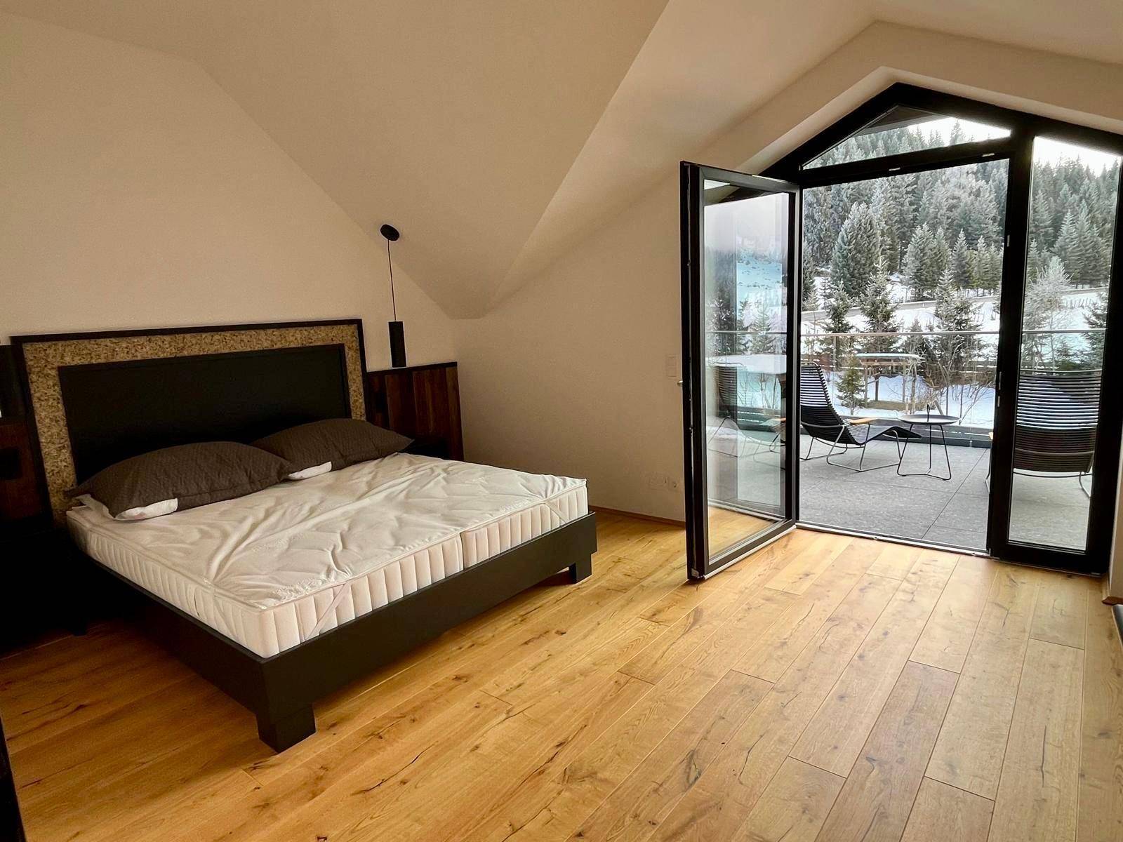 Helles Schlafzimmer mit Holzboden, Dachschräge und Zugang zu einer Terrasse mit Bergblick.
