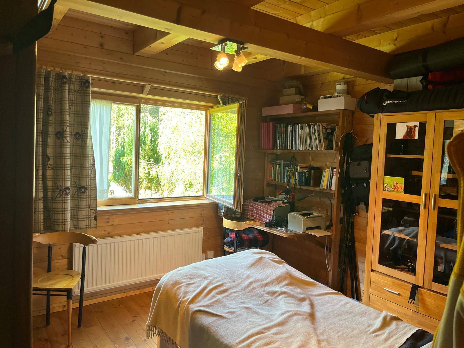 Helles Schlafzimmer mit Holzboden, großem Fenster und Blick ins Grüne.