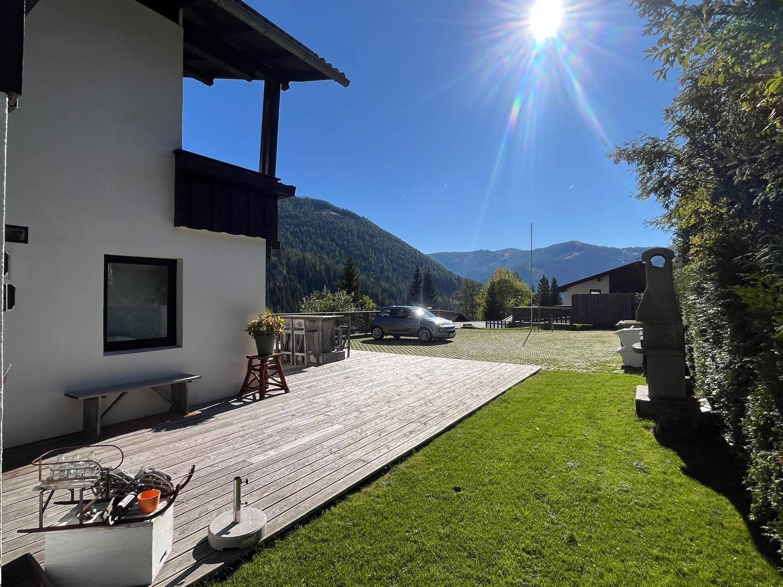 Sonnige Holzterrasse mit angrenzendem Rasen und weitem Blick auf die umliegenden Berge.