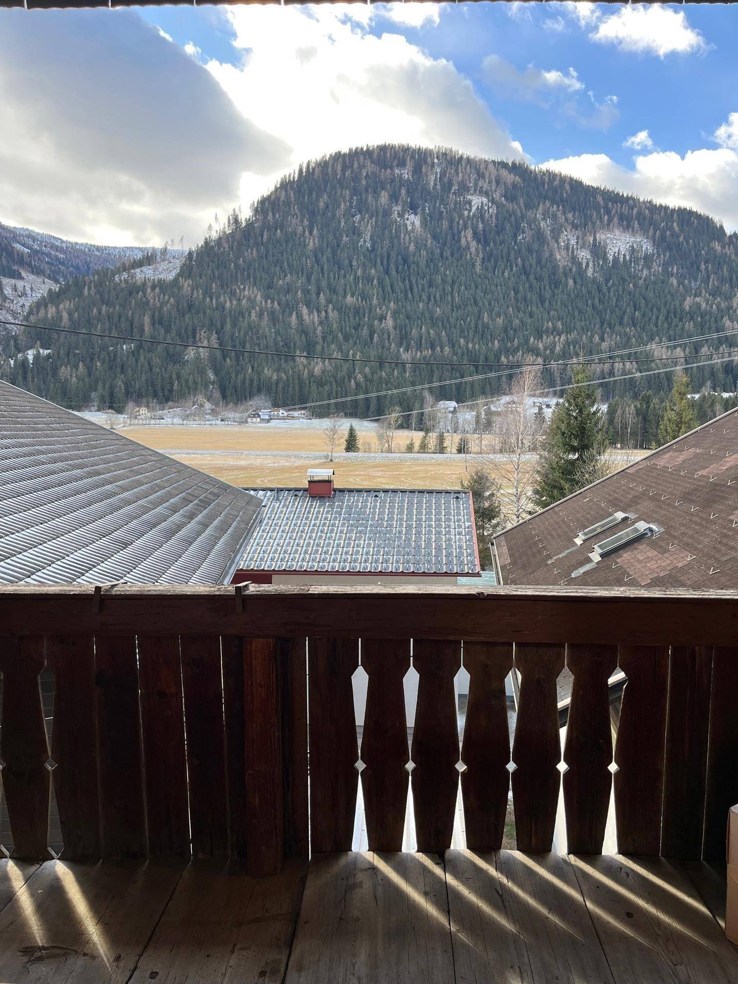 Sonniger Balkon mit Holzbalkonbrüstung und weitem Blick auf die umliegenden Berge und Täler.