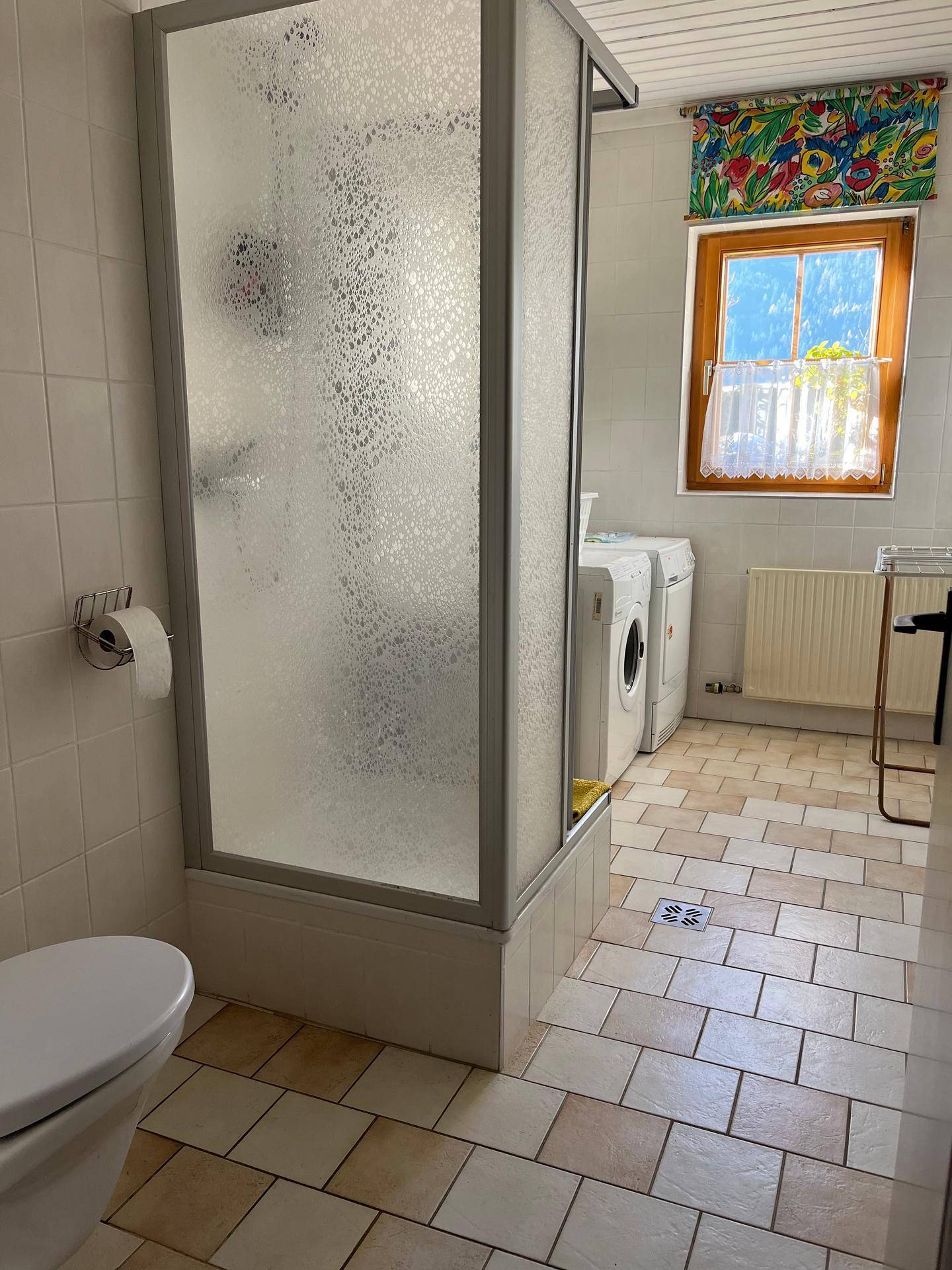 Helles Badezimmer mit Duschkabine, WC, Waschmaschine und Trockner, ausgestattet mit Fliesenboden.