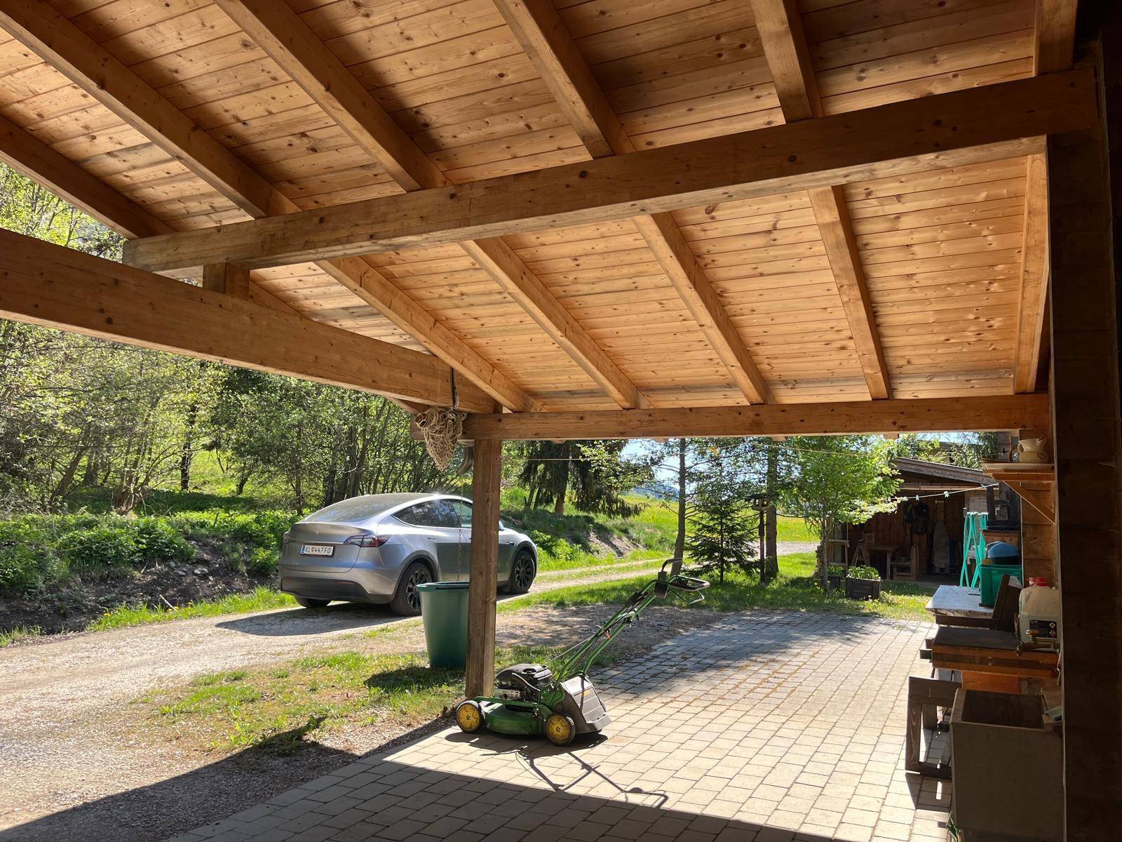 Offener Carport mit Holzdach und gepflastertem Boden, bietet Platz für ein Fahrzeug.