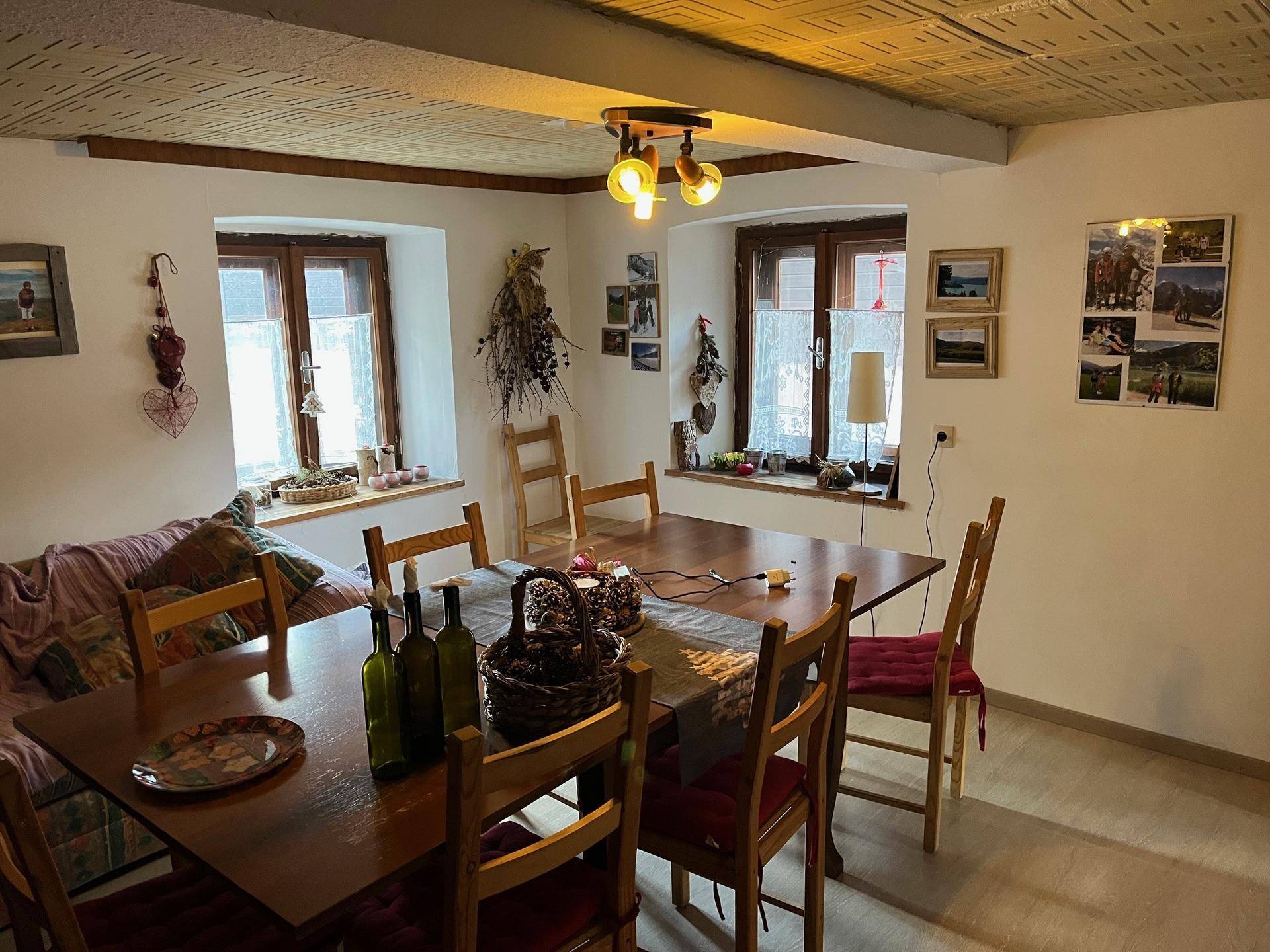 Rustikaler Essbereich mit Holztisch, Stühlen und traditioneller Dekoration, beleuchtet durch kleine Fenster.