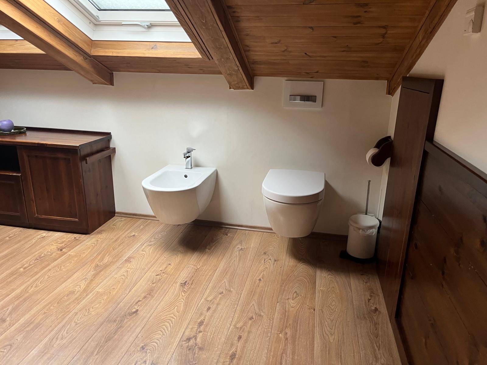 Modernes Badezimmer mit Bidet, wandhängendem WC und Holzboden unter Dachschrägen.