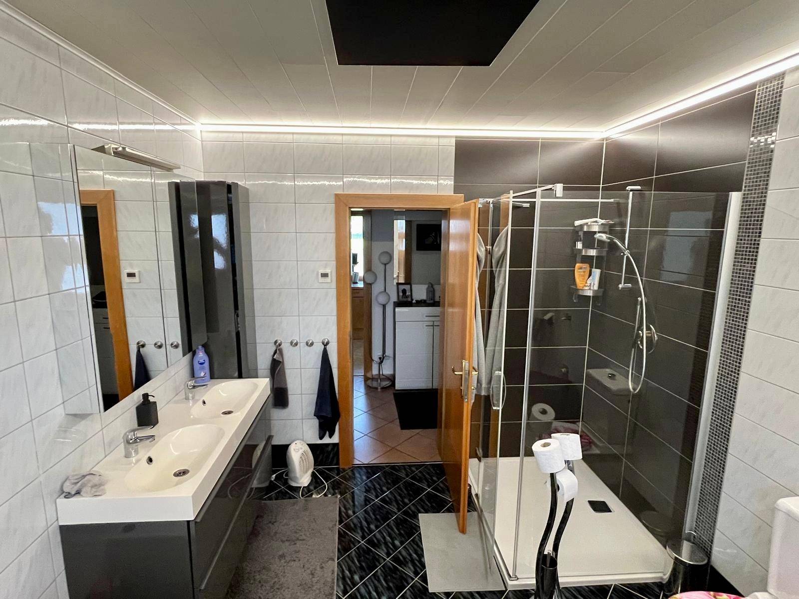 Badezimmer mit begehbarer Dusche, Doppelwaschbecken und modernen Fliesen.