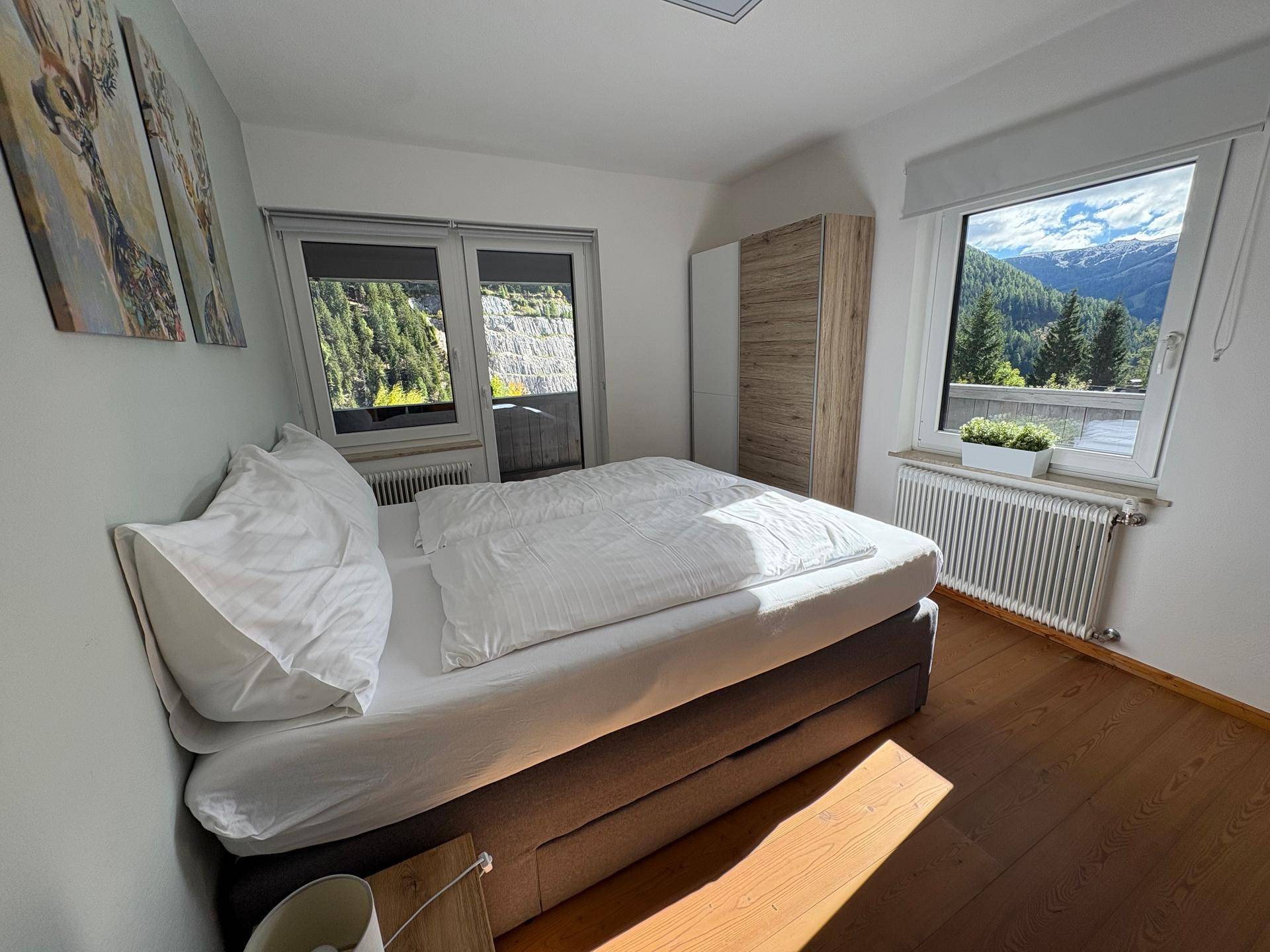 Helles Schlafzimmer mit Doppelbett und zwei Fenstern, die einen wunderschönen Bergblick bieten.