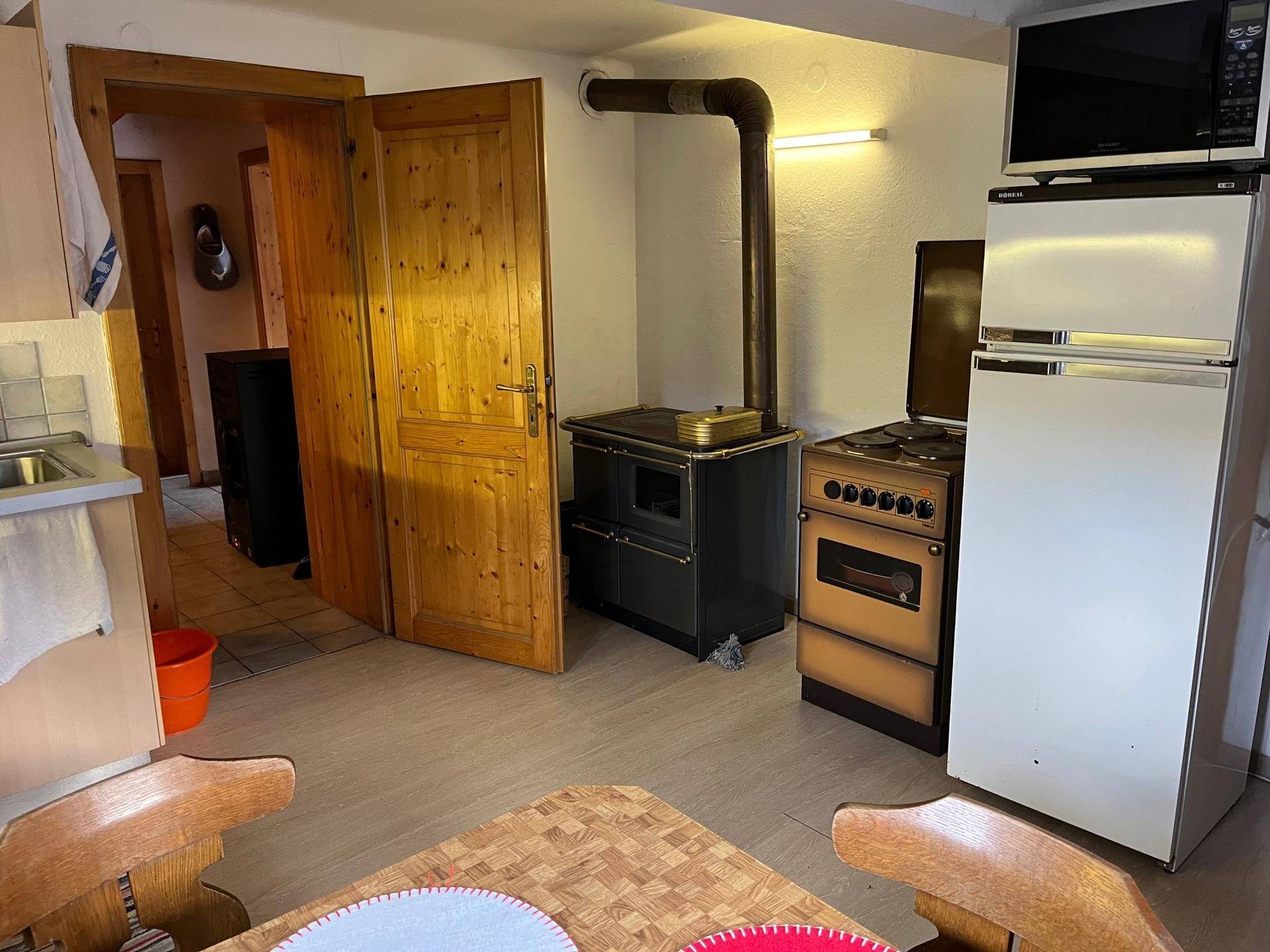 Küchenbereich mit traditionellem Holzofen, Kühlschrank und Mikrowelle, ergänzt durch einen Esstisch.