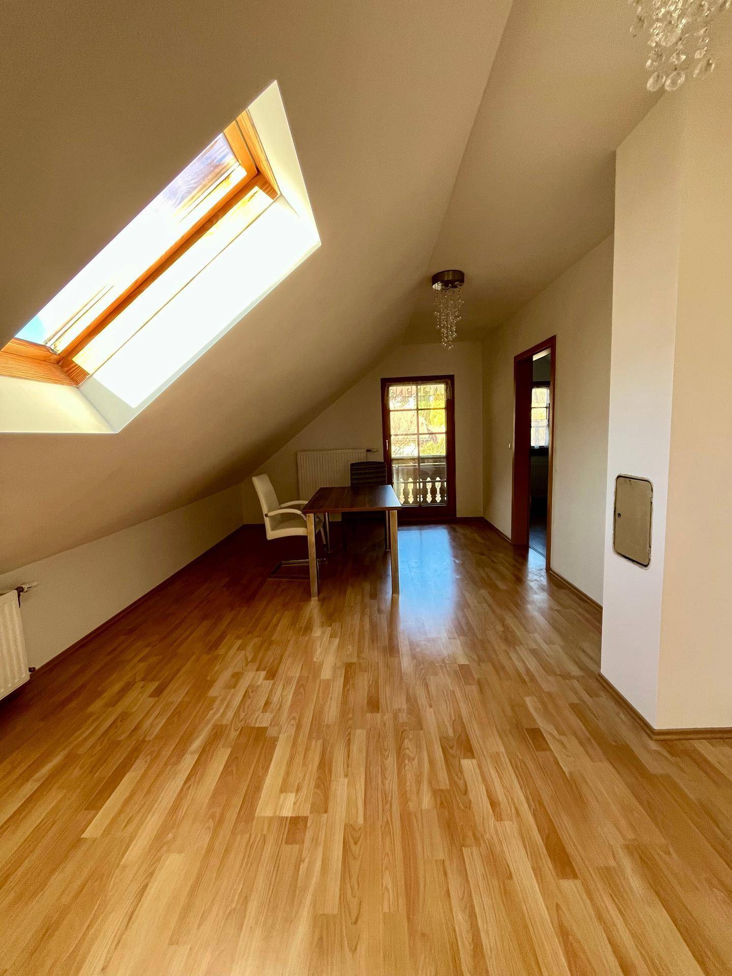 Heller Dachbodenraum mit Laminatboden, Dachfenster und Zugang zu einem Balkon.