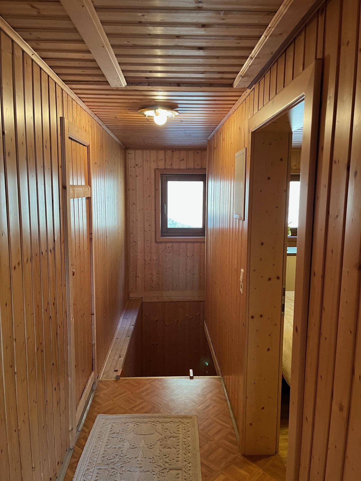 Schmaler Flur mit Holzverkleidung an Wänden und Decke, führt zu einem weiteren Raum.