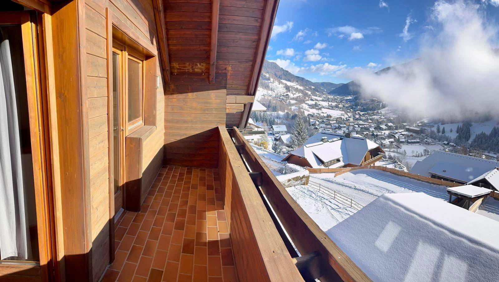 Langer Holzbalkon mit Ziegelboden und atemberaubendem Blick auf das verschneite Tal.