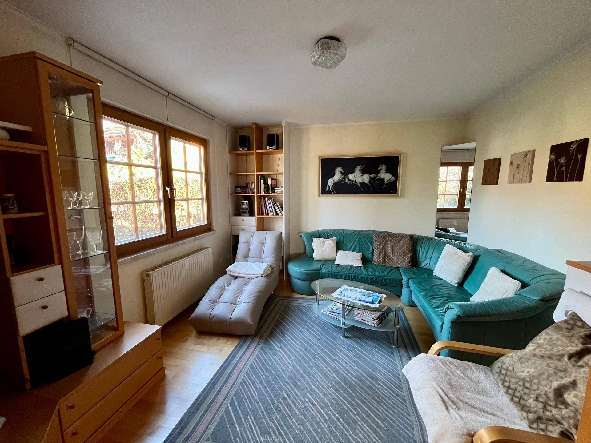 Wohnzimmer mit beiger Wandfarbe, Teppich und einer grünen Ledercouch.
