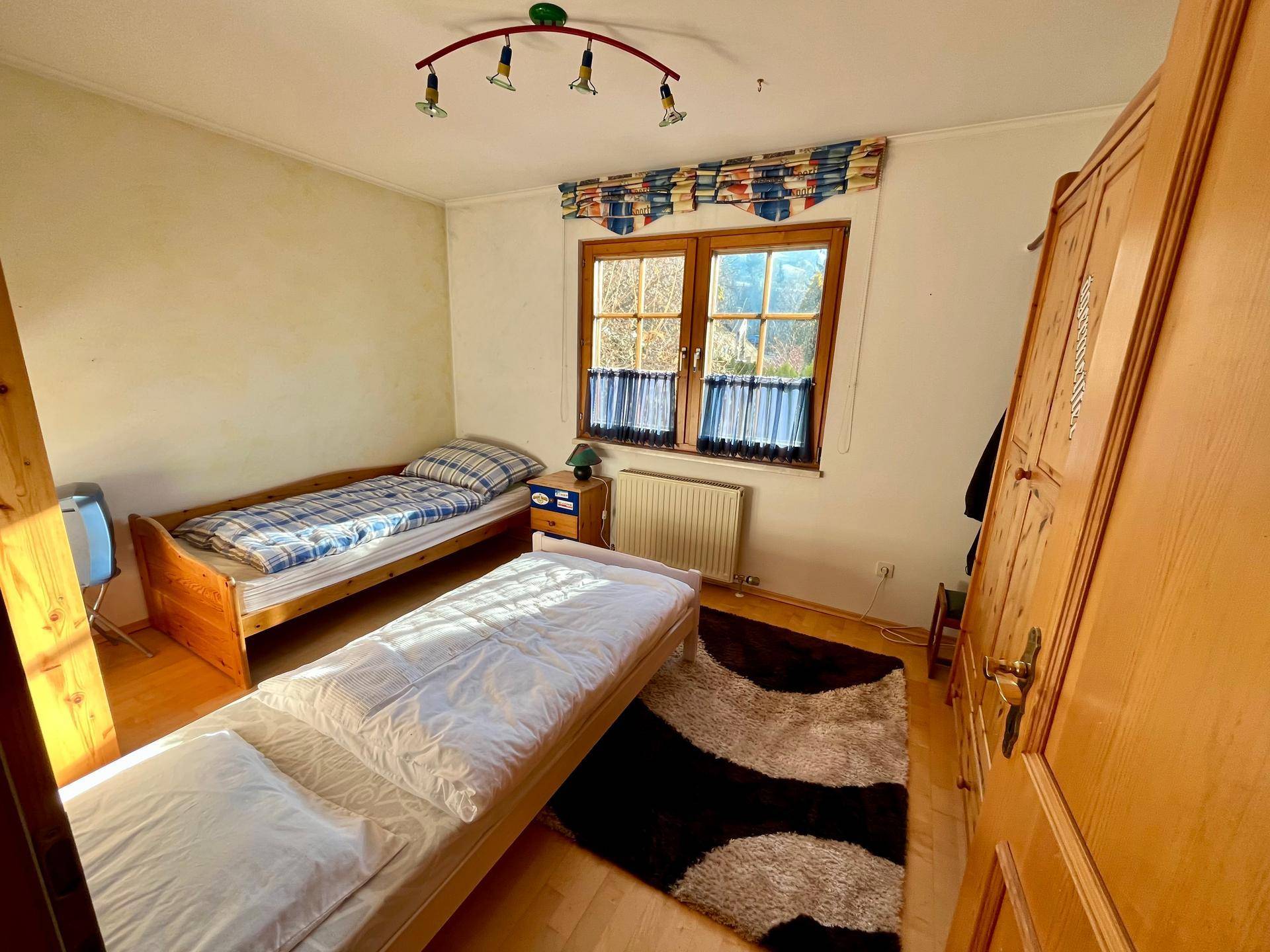 Kinderzimmer mit zwei Einzelbetten, Holzschrank und Fenster mit Blick ins Grüne.