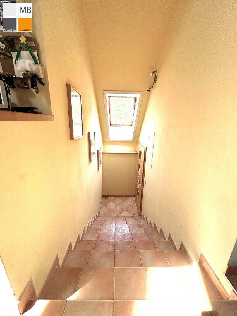 Heller Treppenaufgang mit Fliesenboden und einem Dachfenster, das natürliches Licht spendet.