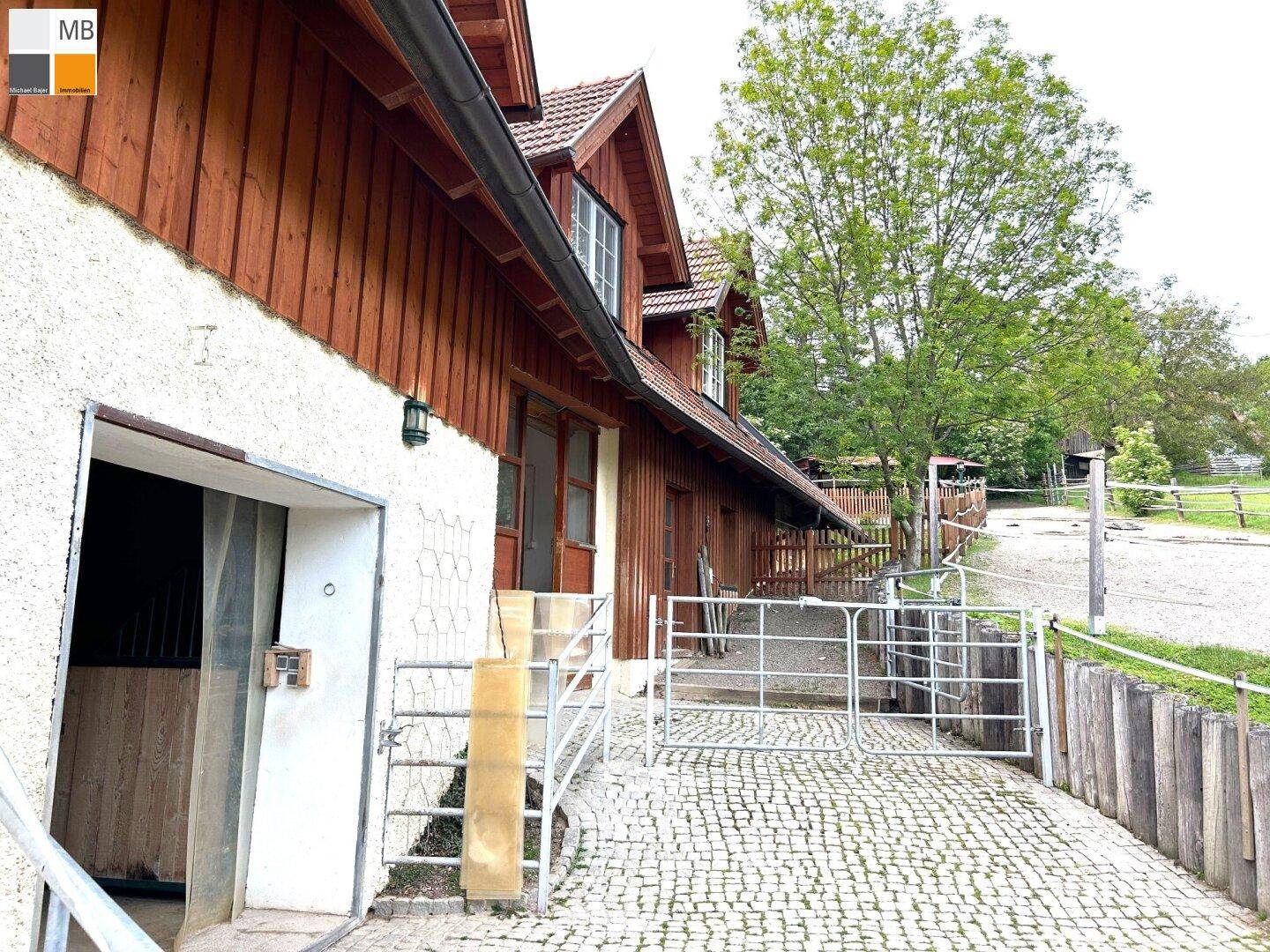 Seitenansicht des Gebäudes mit gepflastertem Weg, Holzelementen und einem eingezäunten Bereich.