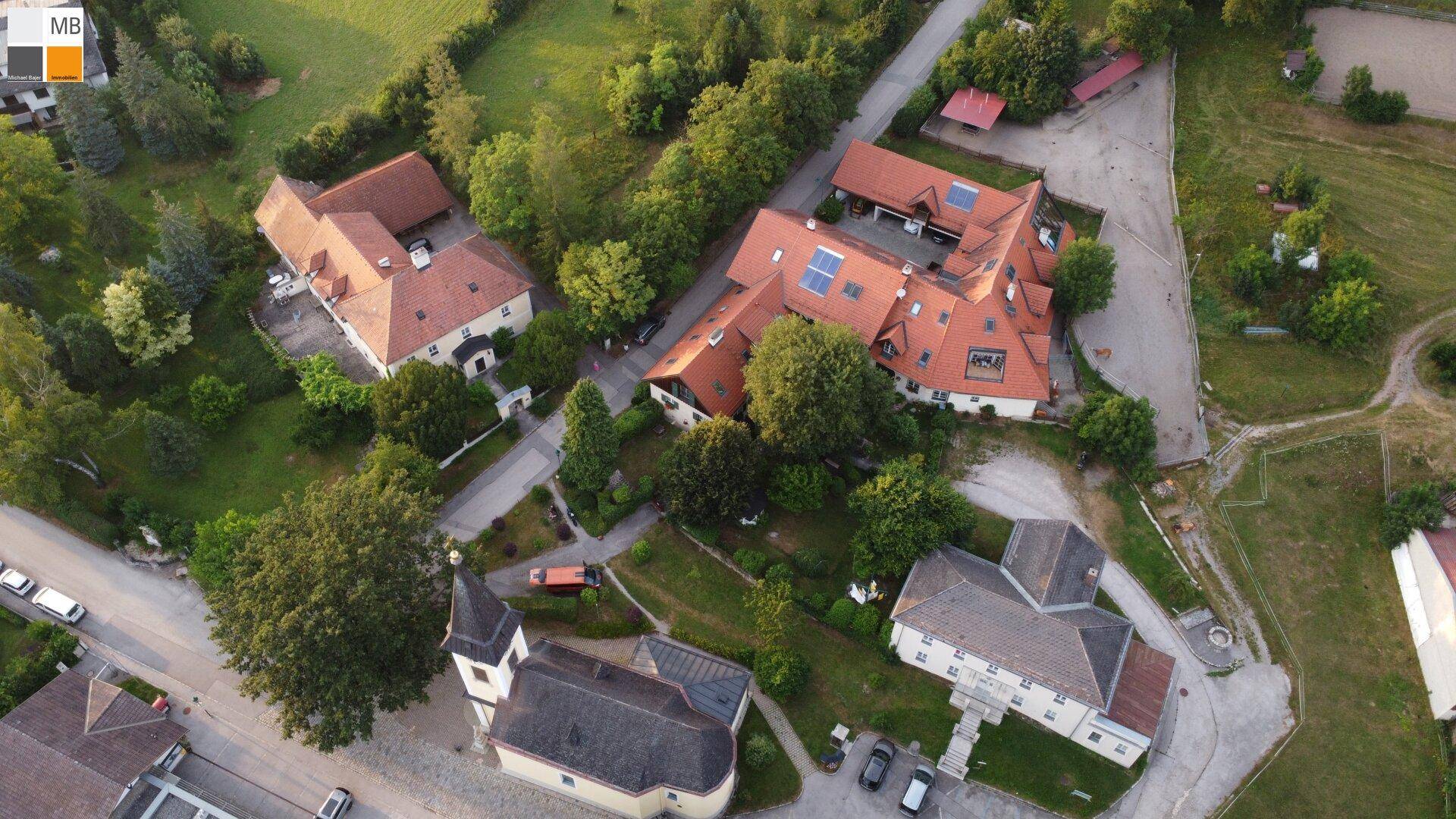 Luftaufnahme einer ländlichen Siedlung mit traditionellen Gebäuden, grünen Wiesen und Bäumen.