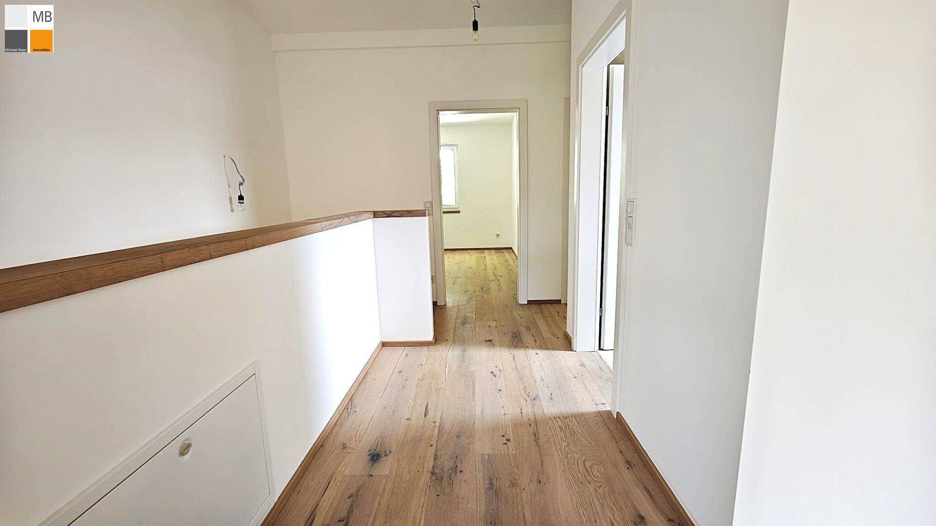 Geräumiger Flur mit Holzboden und weiß gestrichenen Wänden, der zu den oberen Räumen führt.