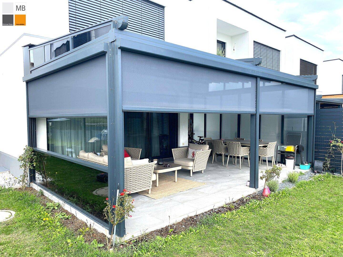 Überdachte Terrasse mit ausgefahrenen Sonnenrollos, bietet Schutz und Privatsphäre im Freien.
