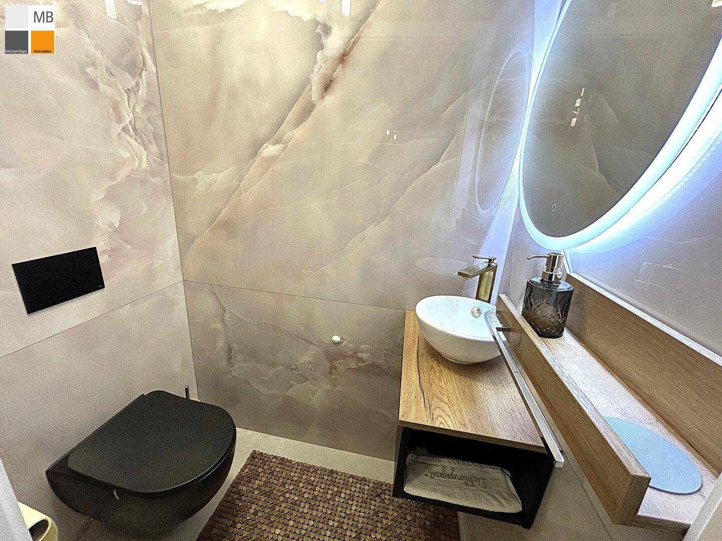 Stilvolles Gäste-WC mit modernem Waschtisch, beleuchtetem Spiegel und dunklem WC.