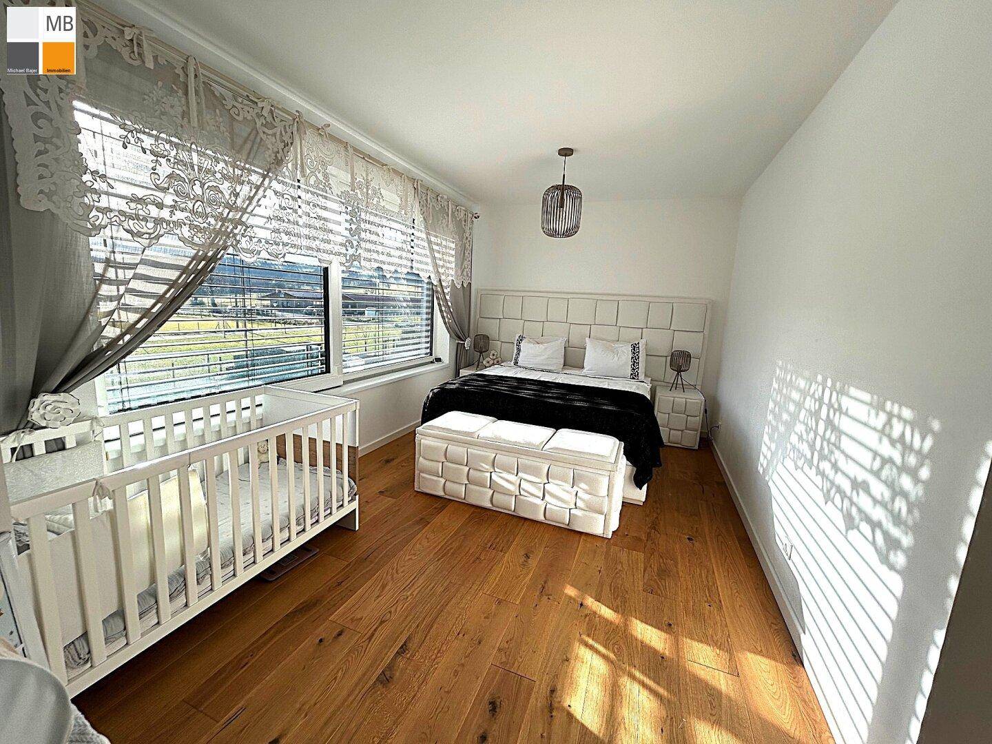 Sonnenverwöhntes Schlafzimmer mit Holzboden, großem Fenster und gemütlicher Atmosphäre.