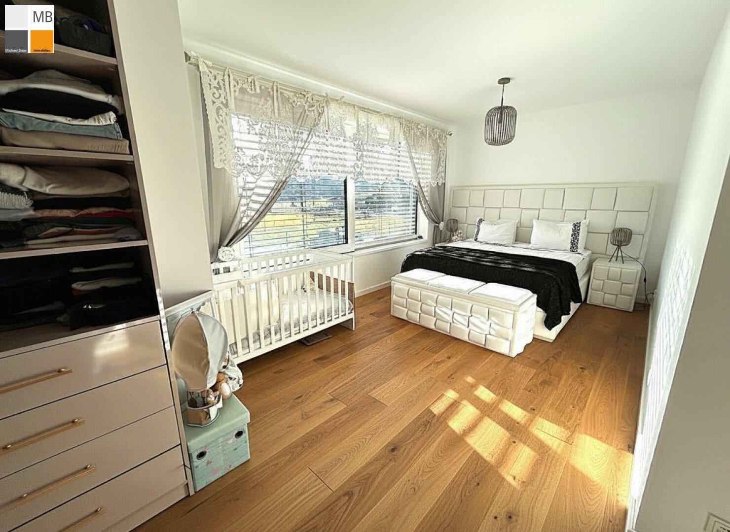 Helles Schlafzimmer mit Holzboden, großem Bett, Babybett und Blick ins Grüne.