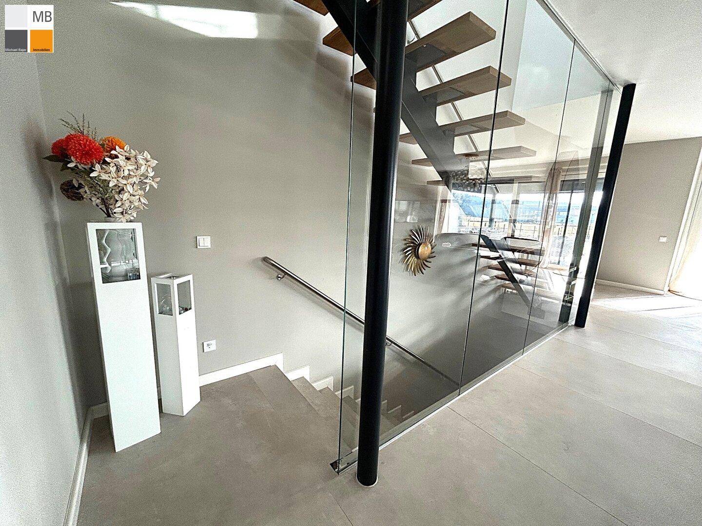 Elegante Treppe mit Glasgeländer und Holzstufen, die die verschiedenen Ebenen des Hauses verbindet.