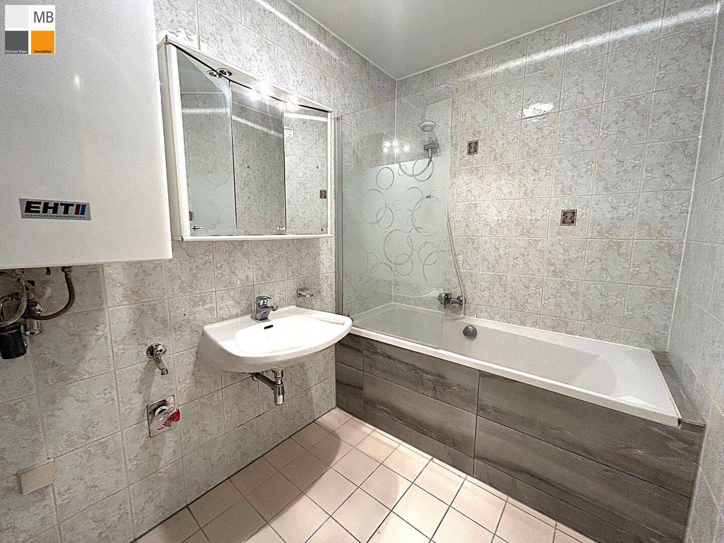 Badezimmer mit Badewanne, Waschbecken und gefliesten Wänden in hellem Grau.