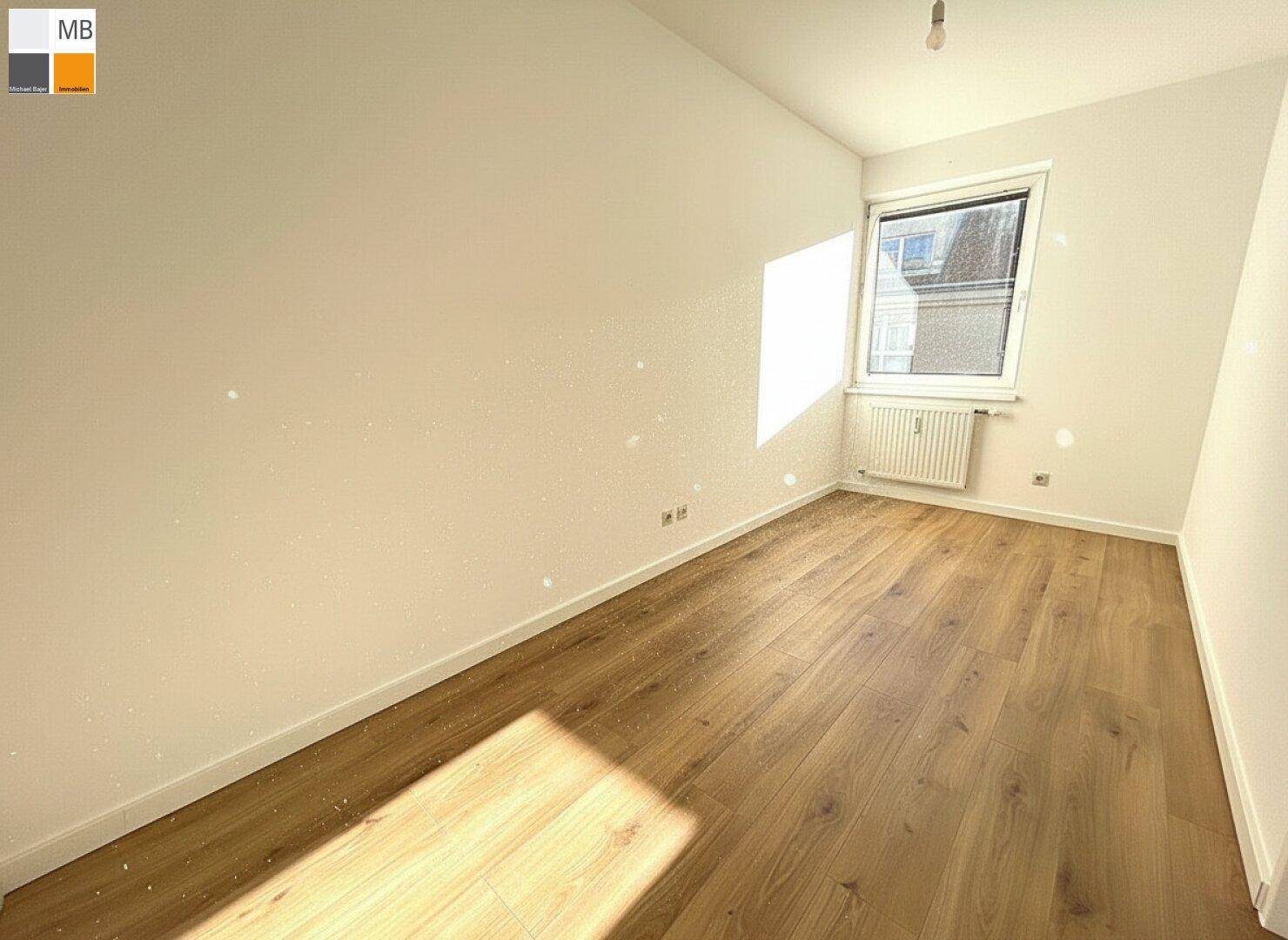Helles Zimmer mit Laminatboden und viel Tageslicht durch das Fenster.