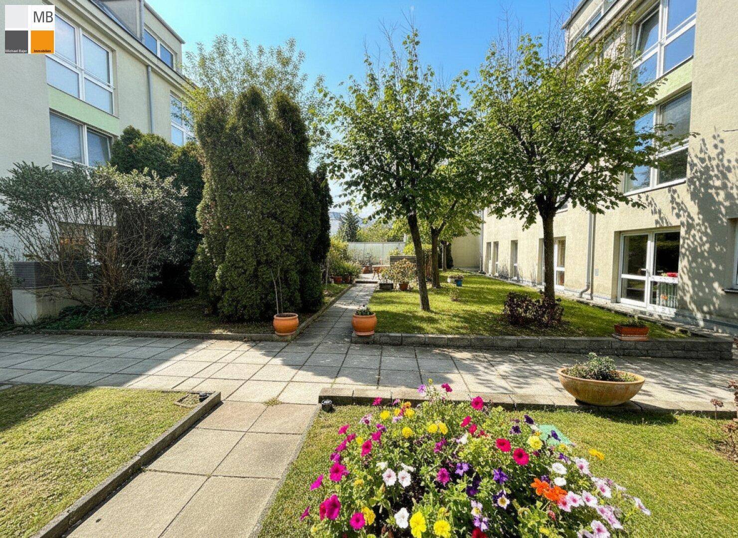 Sonniger Gemeinschaftsgarten mit gepflasterten Wegen und farbenfrohen Blumenarrangements.