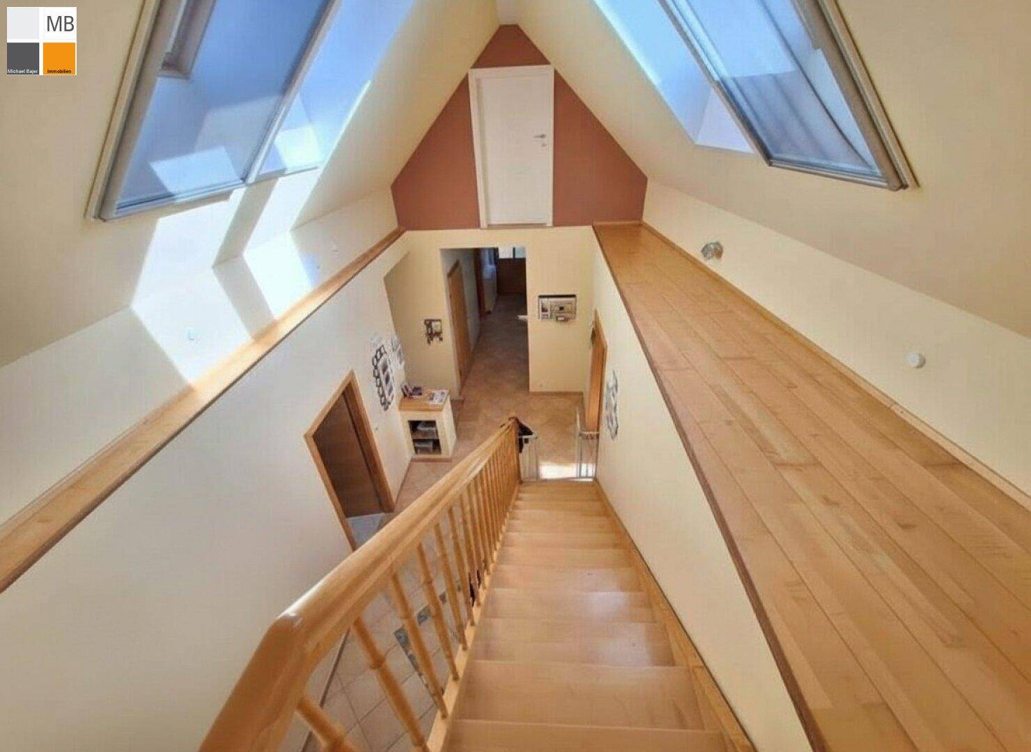 Helle Holztreppe führt ins Obergeschoss mit Dachfenstern und Holzboden.