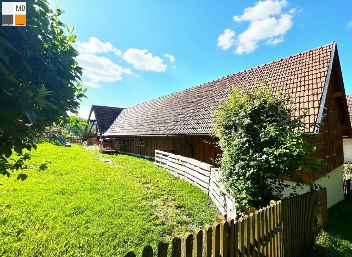 Ländliches Gebäude mit Holzelementen, Ziegeldach und gepflegtem Gartenbereich.