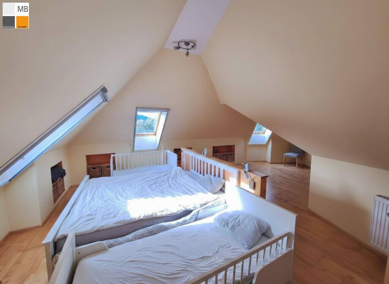 Gemütliches Schlafzimmer im Dachgeschoss mit zwei Betten, Holzboden und Dachfenstern.