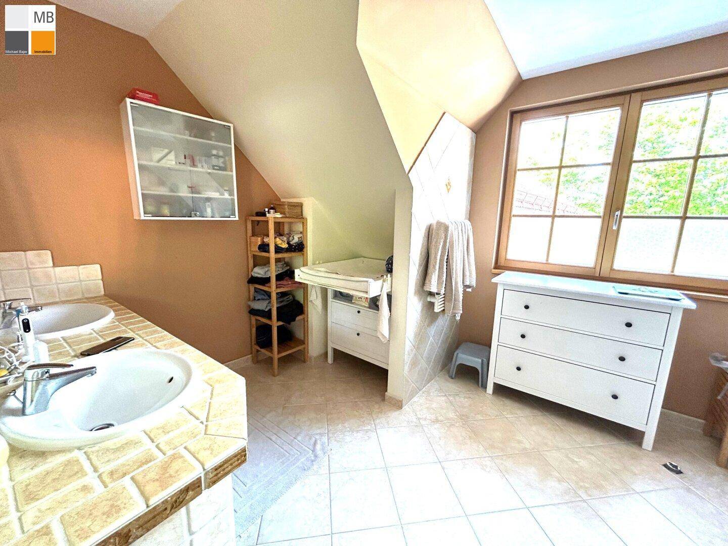 Geräumiges Badezimmer mit Doppelwaschbecken, Fenster und schrägen Wänden im Dachgeschoss.