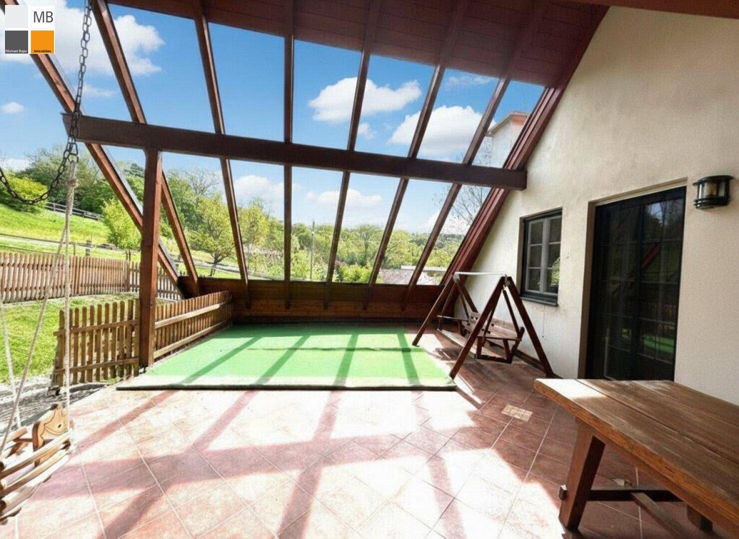 Große überdachte Terrasse mit Schaukel und Blick auf die grüne Umgebung.