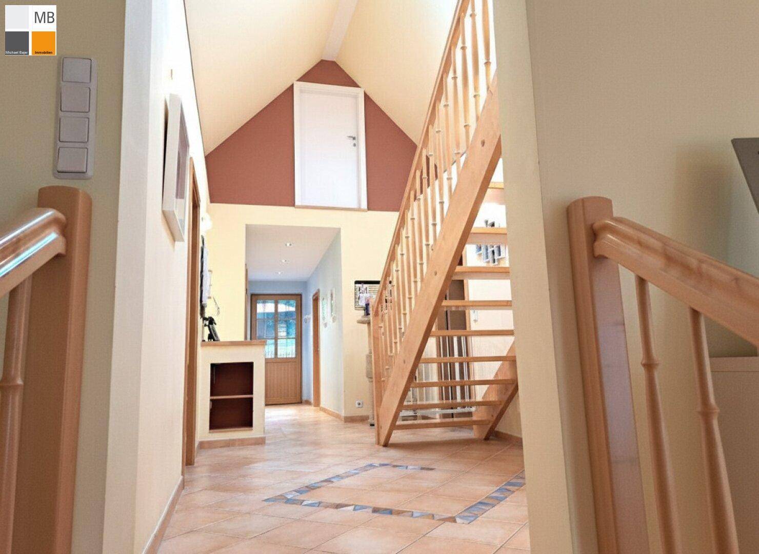 Heller Flur mit Holztreppe, Fliesenboden und hohen Decken, der zu weiteren Räumen führt.