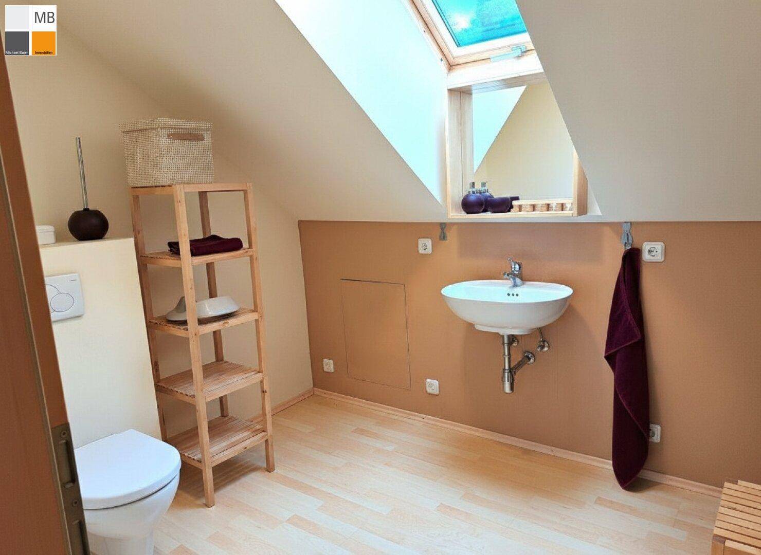 Kleines Gäste-WC mit Waschbecken, Toilette, Holzboden und Dachfenster.