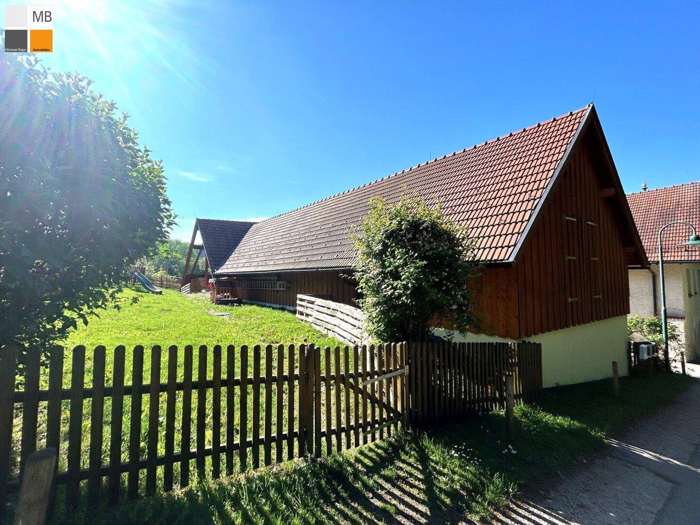Ländliches Gebäude mit Holzelementen, Ziegeldach und sonnigem Gartenbereich.