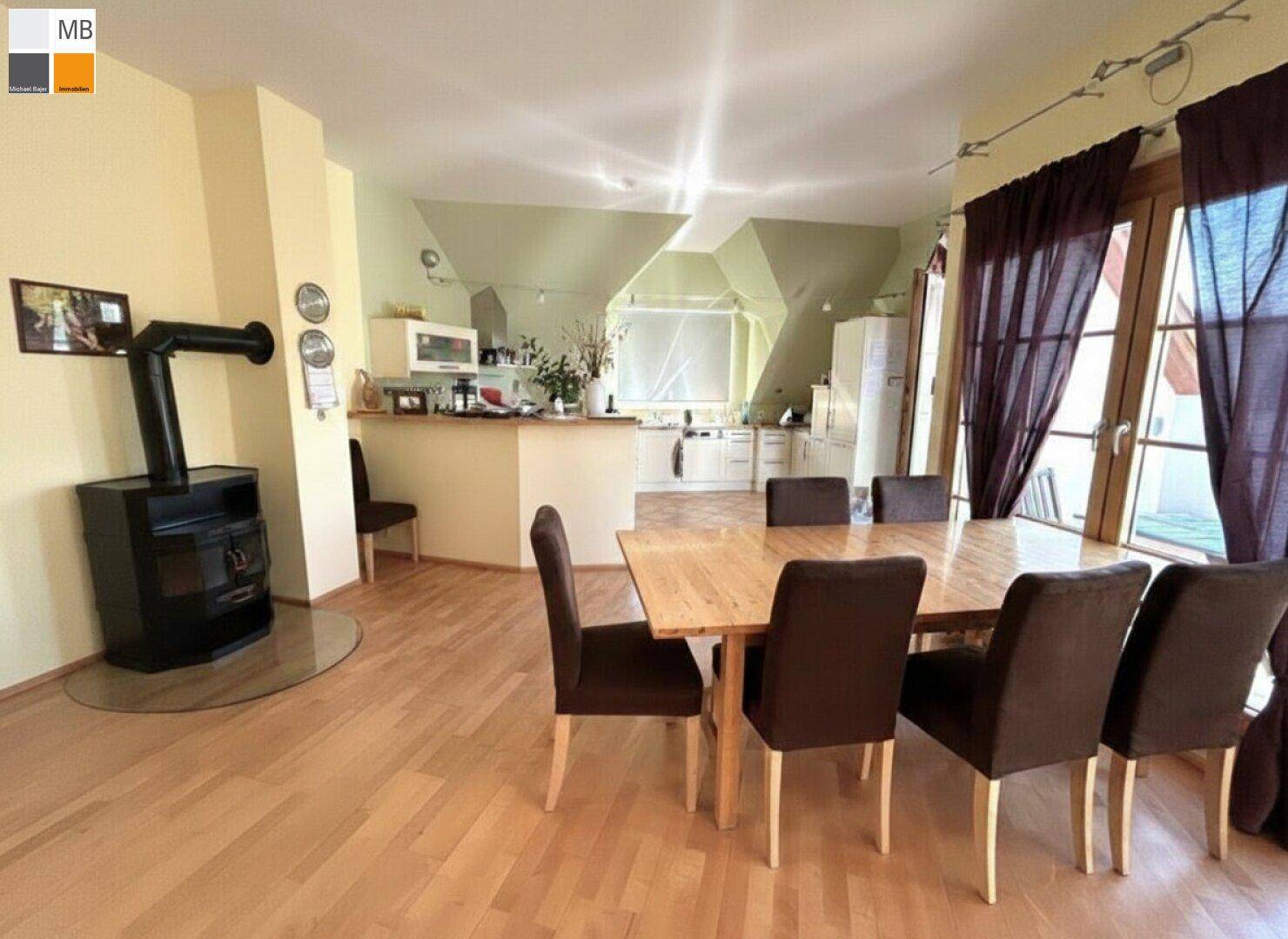 Heller Essbereich mit Holztisch, Stühlen und einem modernen Holzofen im Hintergrund.