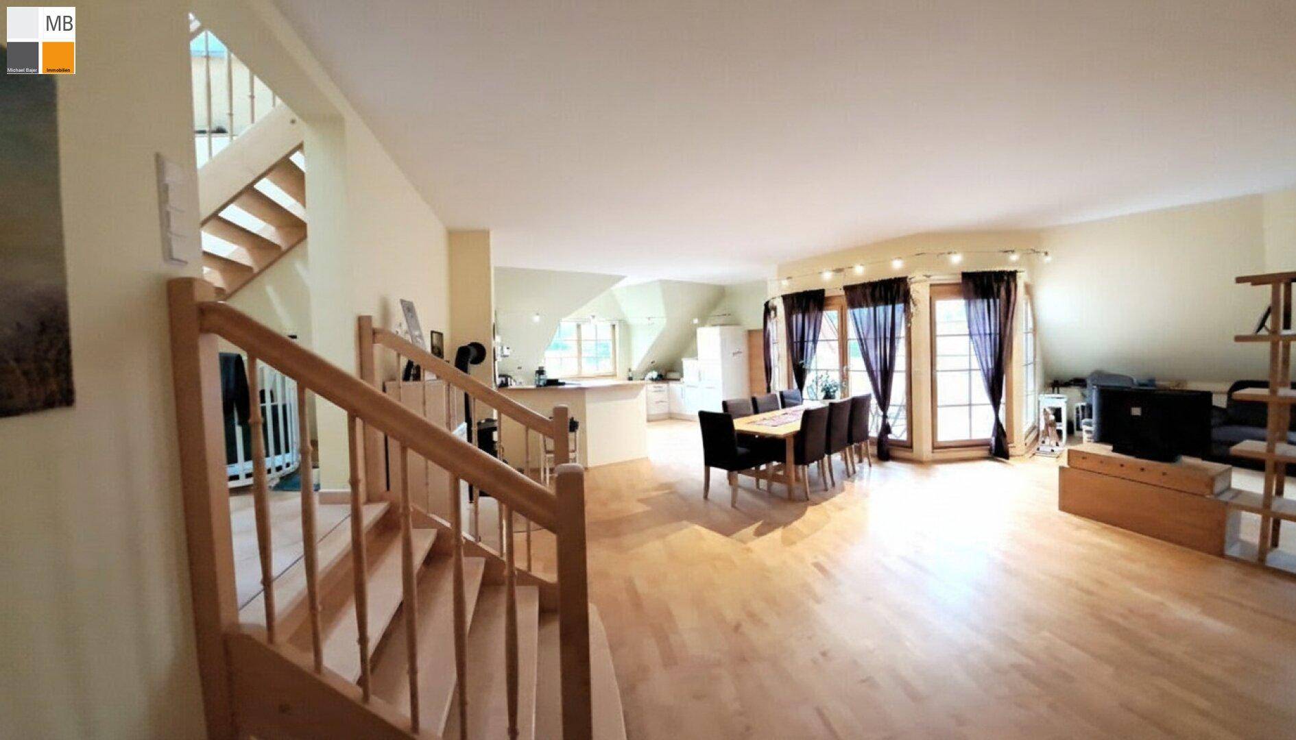 Großzügiger Wohn-Essbereich mit Holztreppe, Parkettboden und Zugang zu einem Balkon.