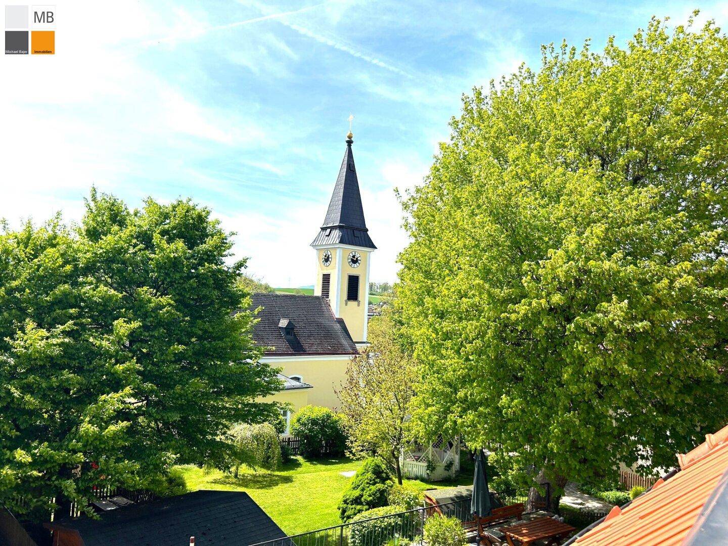 Malerischer Ausblick auf eine Kirche mit grünem Garten und Bäumen unter blauem Himmel.