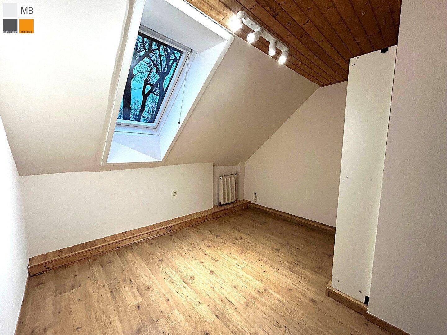 Dachgeschossraum mit Holzboden, Dachfenster und sichtbarer Holzdecke.