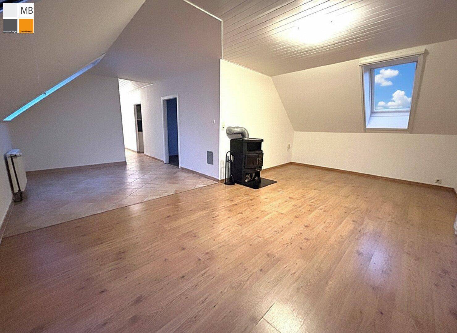 Geräumiger Wohnbereich im Dachgeschoss mit Holzboden, Kaminofen und Übergang zu Fliesen.