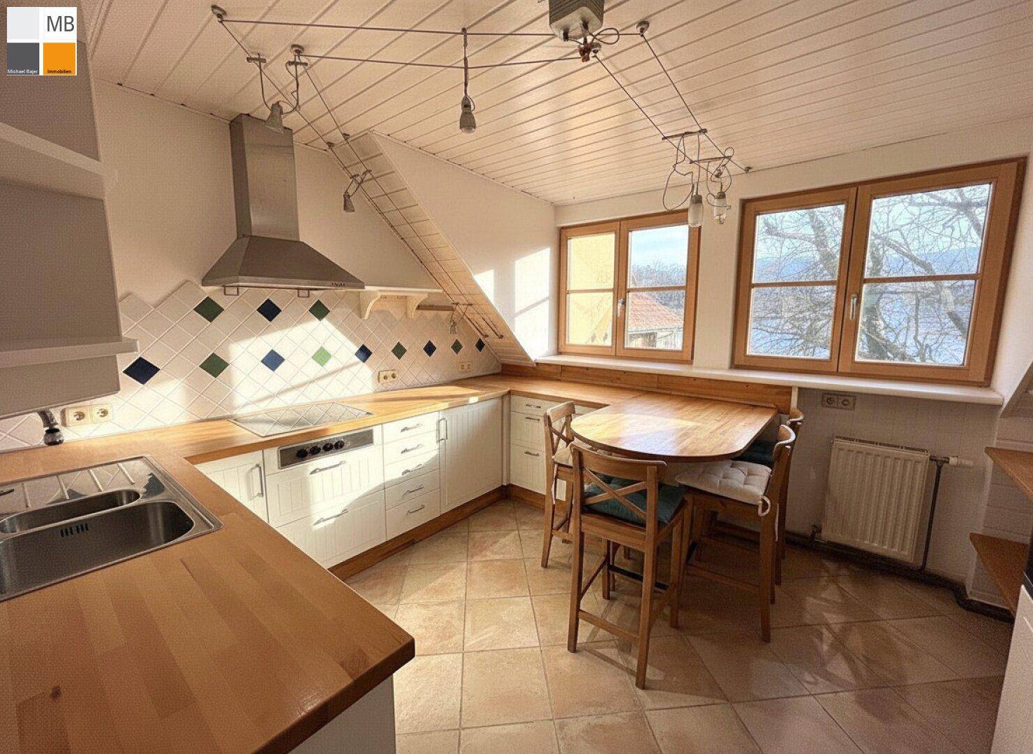 Gemütliche Küche im Dachgeschoss mit Holzarbeitsplatten, Essbereich und großen Fenstern.