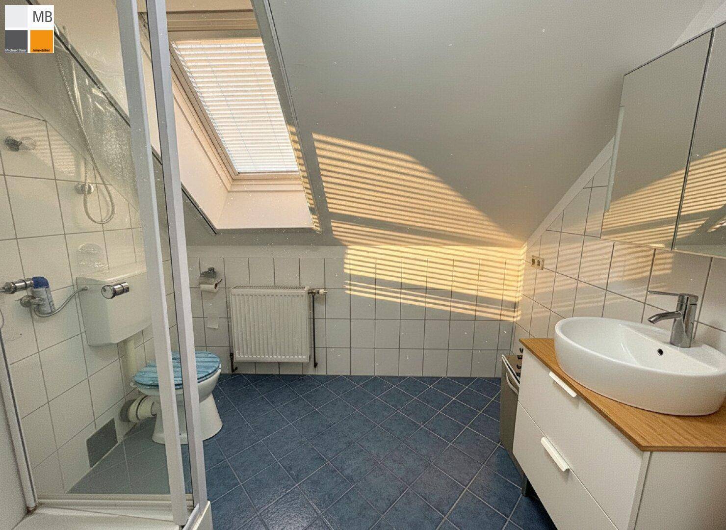 Badezimmer im Dachgeschoss mit blauen Fliesen, Dusche, Waschtisch und Dachfenster.