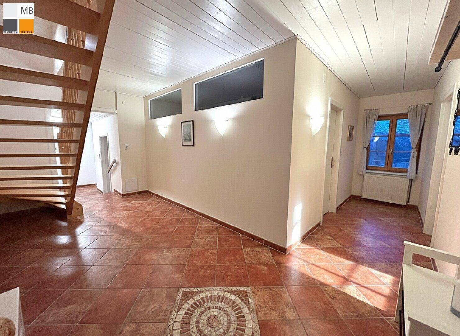 Geräumiger Flur mit Terrakotta-Fliesenboden und einer Holztreppe, die in die oberen Etagen führt.