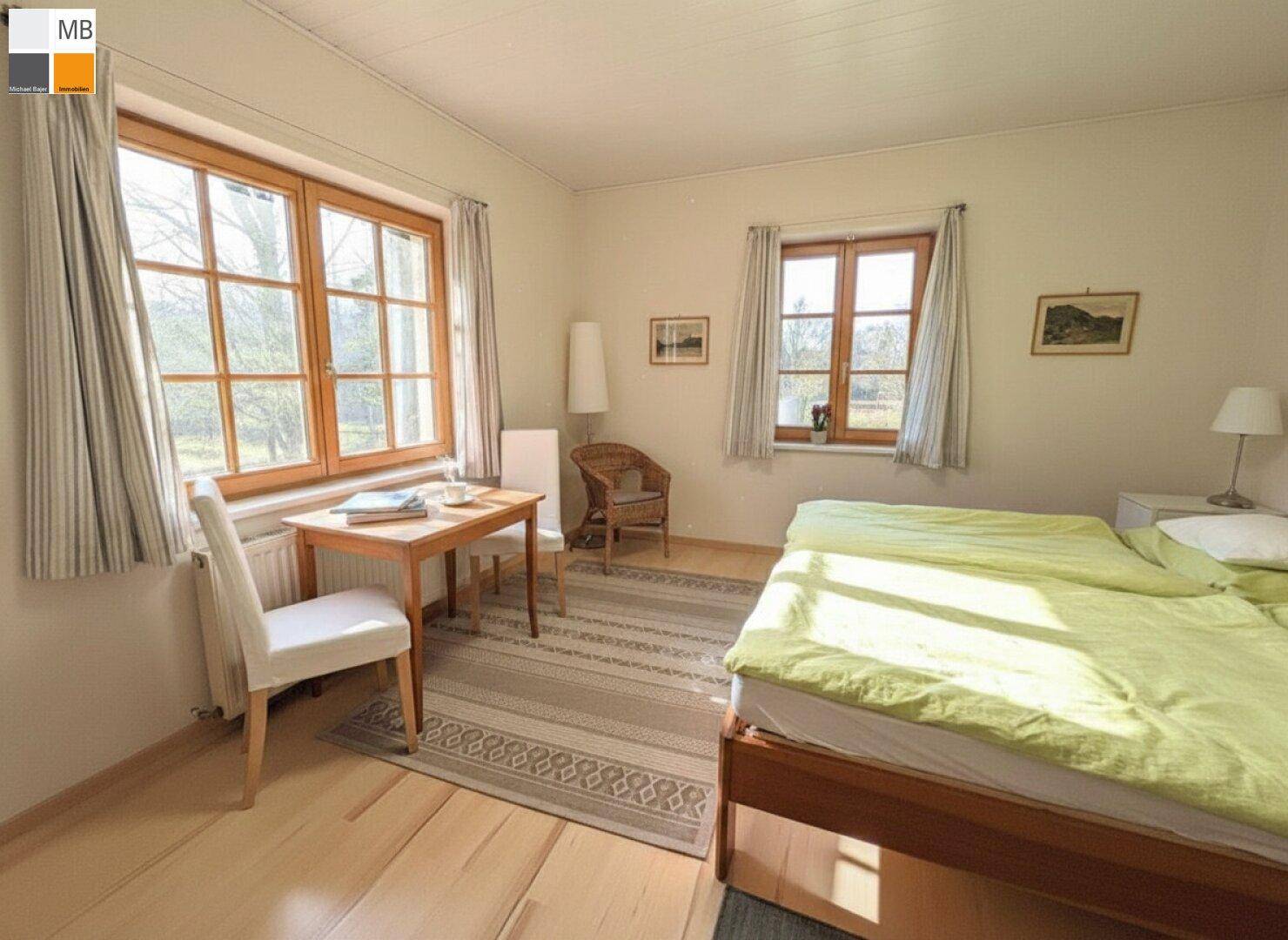 Gemütliches Schlafzimmer mit Holzboden, Doppelbett und zwei Fenstern mit Blick ins Grüne.