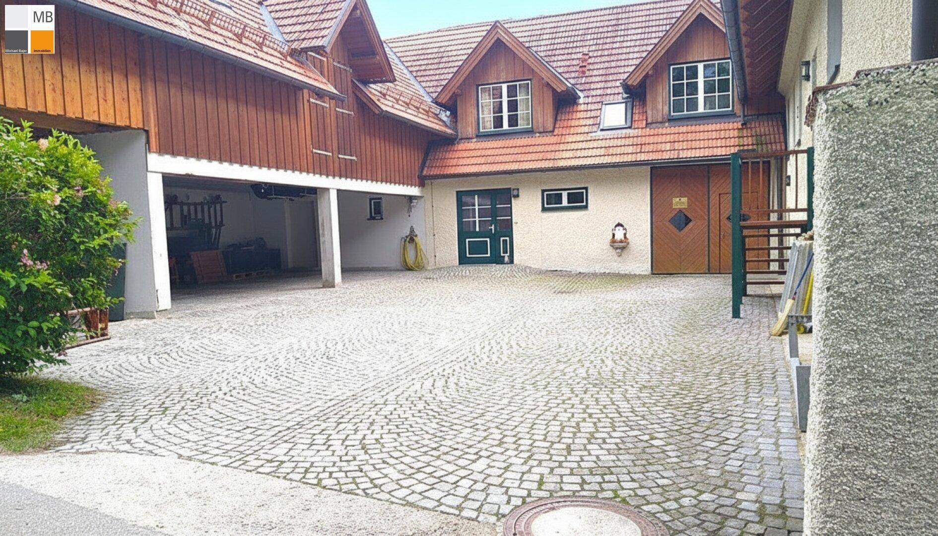 Großer gepflasterter Hofbereich mit Garagen und Nebengebäuden, umgeben von ländlicher Architektur.