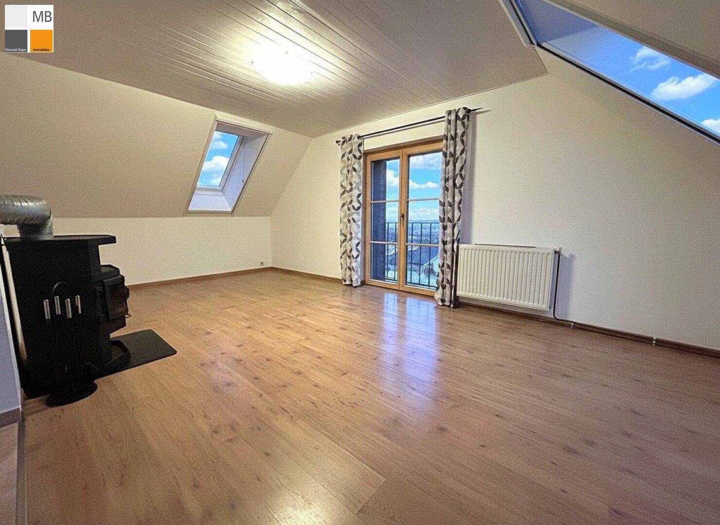 Heller Wohnraum im Dachgeschoss mit Holzboden, Kaminofen und Zugang zu einem Balkon.